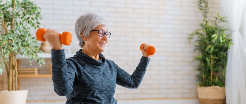 Older woman with short hair holding up a pair of orange dumbells